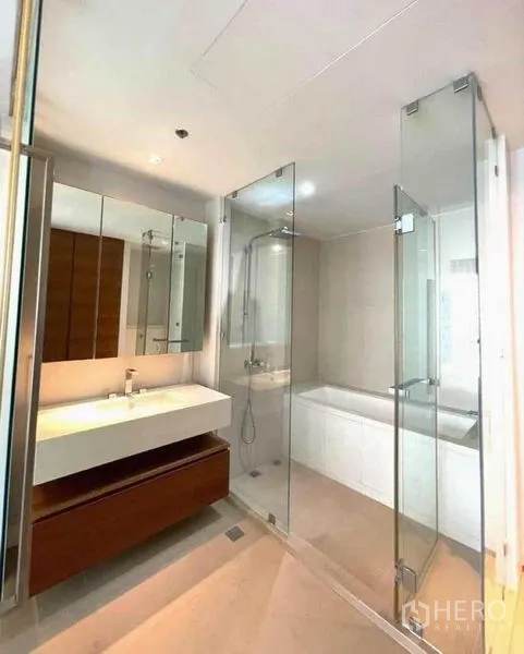 Condominium for rent in Khlong San, Bangkok - Bathroom with mirrored cabinets, glass shower enclosure and bathtub.