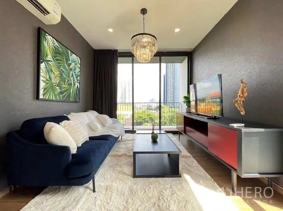 公寓 for rent in Watthana, Bangkok - 客厅有海军蓝沙发、吊灯与电视柜，落地玻璃通向阳台。