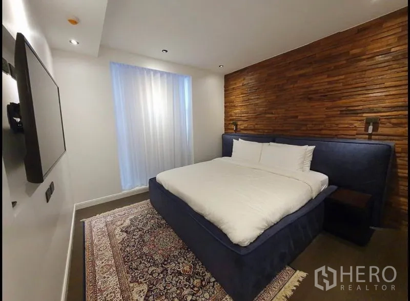 Condominium for rent in Watthana, Bangkok - Cozy bedroom with wood feature wall, large bed and soft ambient lighting.