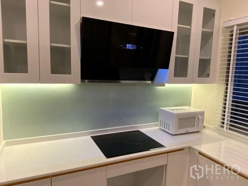 Townhouse for rent in Prawet, Bangkok - Close-up of sleek cooktop, range hood and lighted glass backsplash in the kitchen.