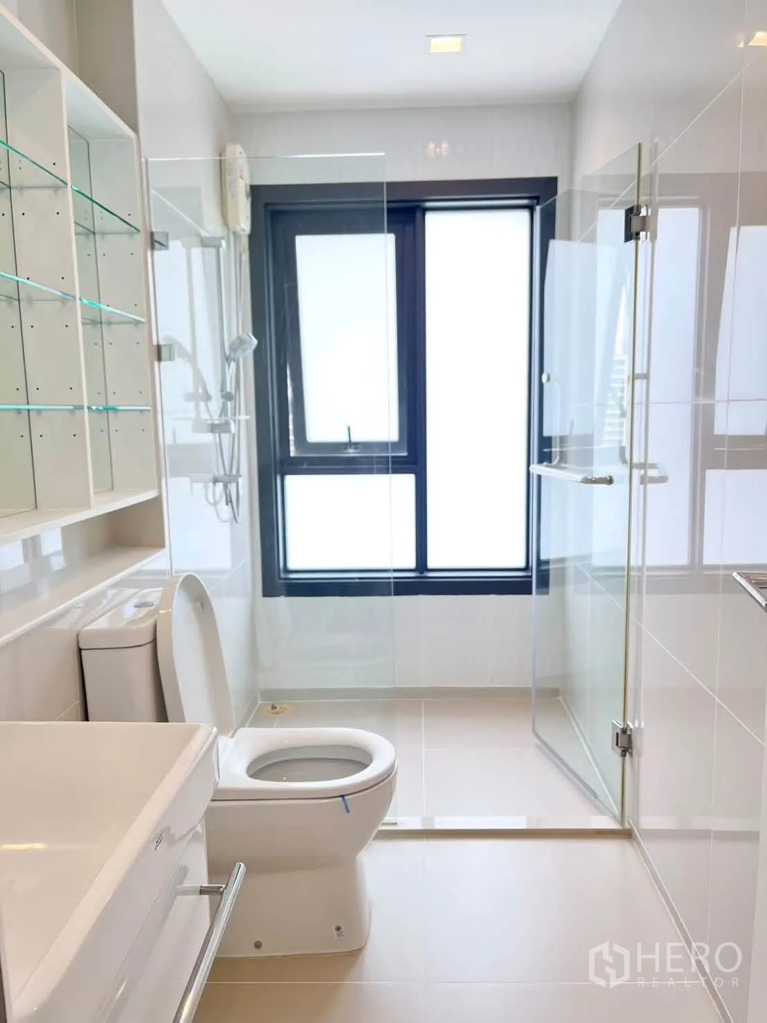 Condominium for rent in Pathum Wan, Bangkok - Bright bathroom with glass shower enclosure, toilet, and frosted window.
