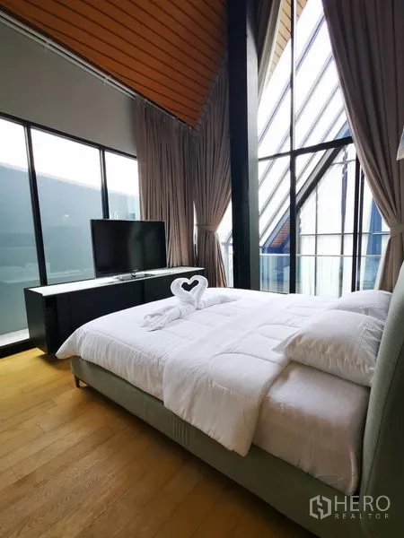 Apartment for rent in Khlong Toei, Bangkok - Bright bedroom with floor-to-ceiling windows, TV console, and soft bedding.