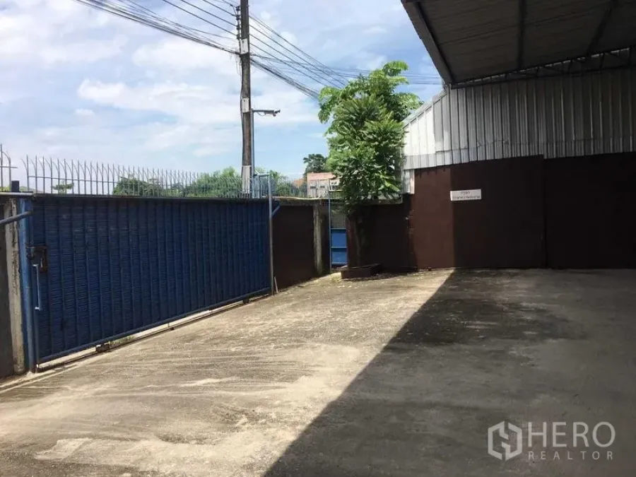 Warehouse for rent in Bueng Kum, Bangkok - Gated loading yard with blue sliding gate, perimeter fence and partial roof at the warehouse.