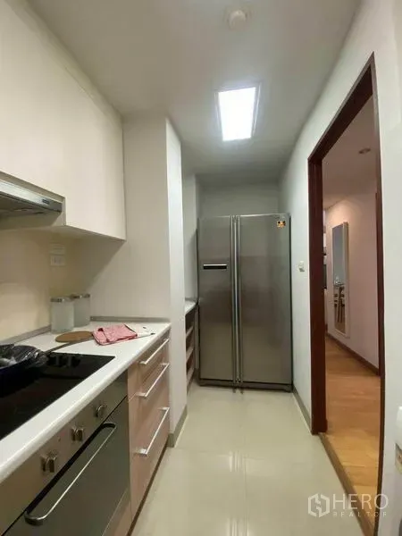 公寓 出租或出售在Phra Khanong, Bangkok - 紧凑走廊式厨房，配灶具、烤箱、排烟机和不锈钢双门冰箱。