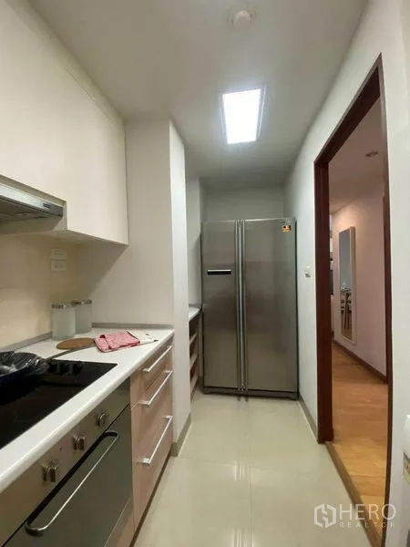 公寓 出租或出售在Phra Khanong, Bangkok - 紧凑走廊式厨房，配灶具、烤箱、排烟机和不锈钢双门冰箱。