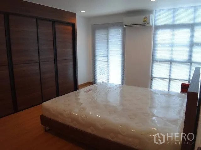 Condominium for rent in Bang Rak, Bangkok - Bedroom featuring a dark wood built-in wardrobe, air conditioning, and large windows for natural light.