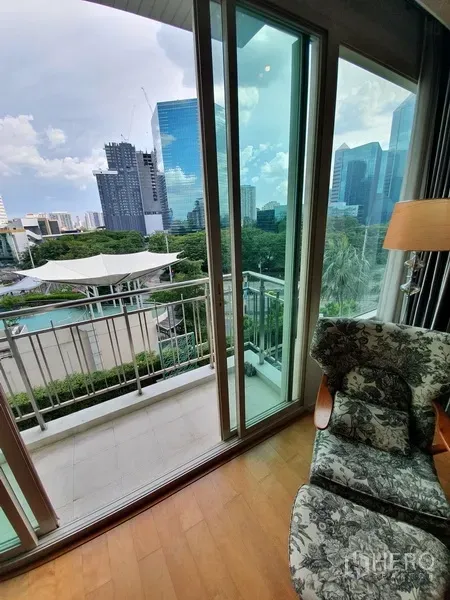 Condominium for rent in Chatuchak, Bangkok - Close view of balcony and sliding doors beside an armchair, overlooking the pool, greenery and skyline.