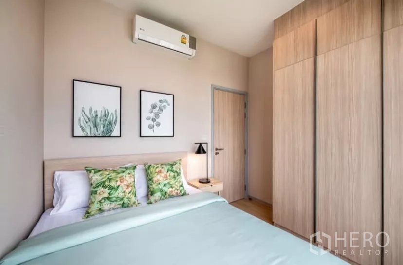 Condominium for rent in Chatuchak, Bangkok - Second bedroom with double bed, botanical accents, built-in wardrobe and air conditioner.