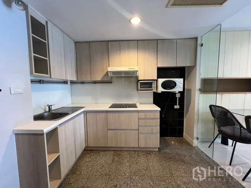 Condominium for rent or sale in Khlong Toei, Bangkok - L-shaped kitchen with light wood cabinets, cooktop and range hood.