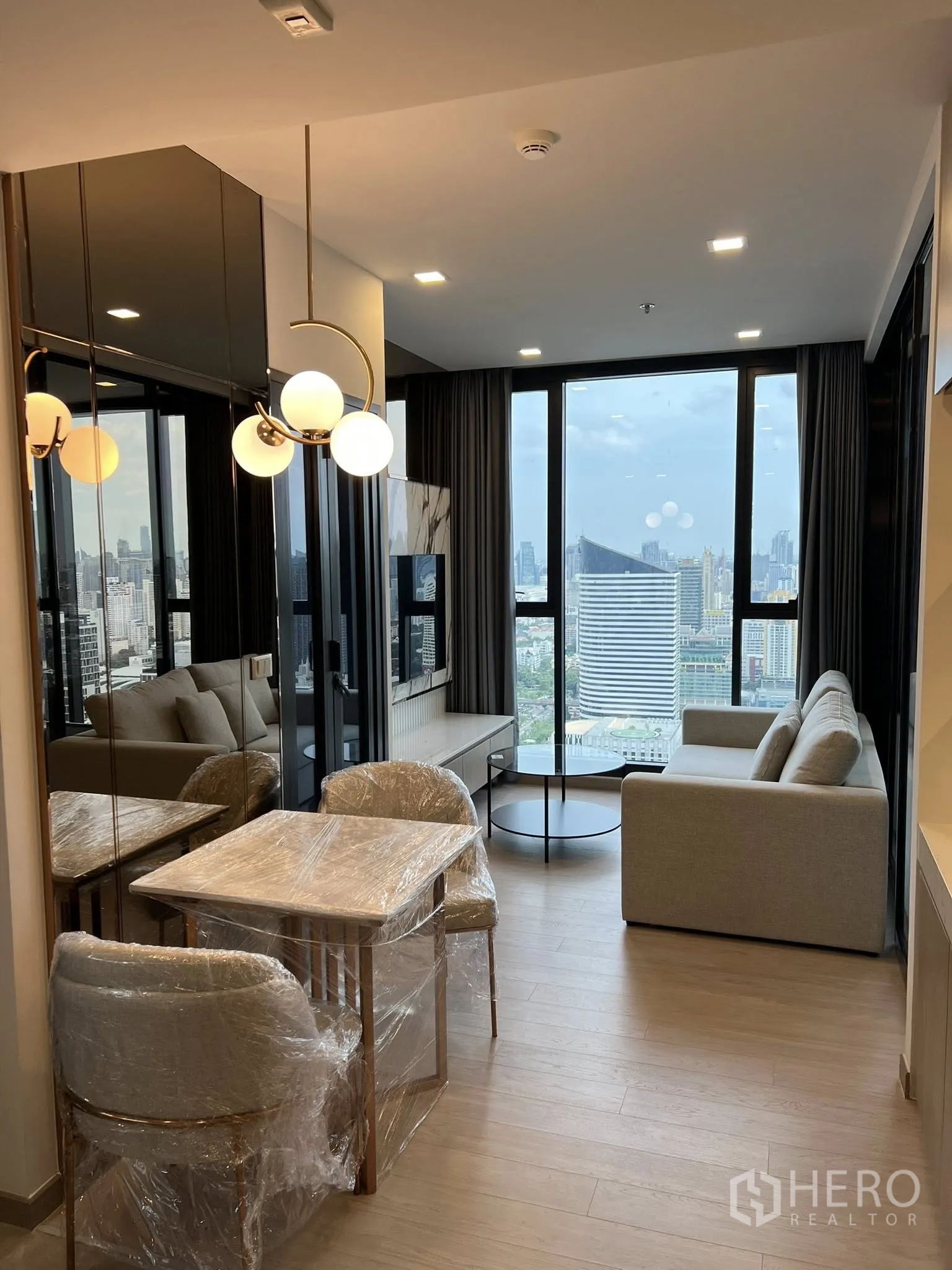 คอนโด for rent in Huai Khwang, Bangkok - มุมทานอาหารและพื้นที่นั่งเล่นหันสู่หน้าต่างบานใหญ่ โต๊ะกลางทรงกลม และผนังทีวีลายหินอ่อนสมัยใหม่