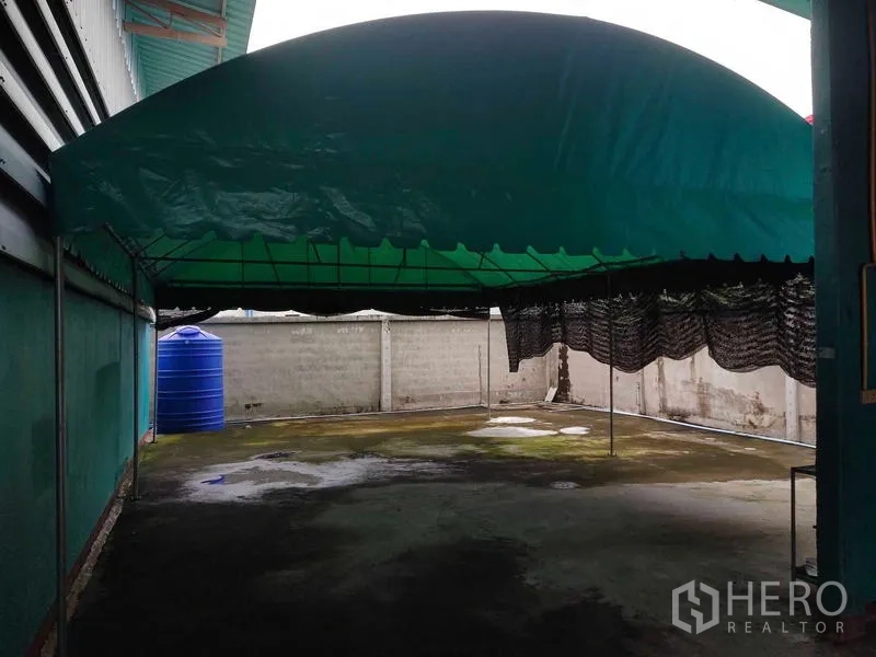 คลังสินค้า ขายในLam Luk Ka, Pathum Thani - พื้นที่กลางแจ้งมีเต็นท์ผ้าใบสีเขียวและแทงก์น้ำสีน้ำเงินติดกำแพง