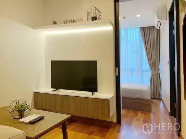 คอนโด ขายในRatchathewi, Bangkok - ห้องนั่งเล่นชั้นวางทีวีลอยพื้น พื้นไม้ และประตูบานเลื่อนไปยังห้องนอน