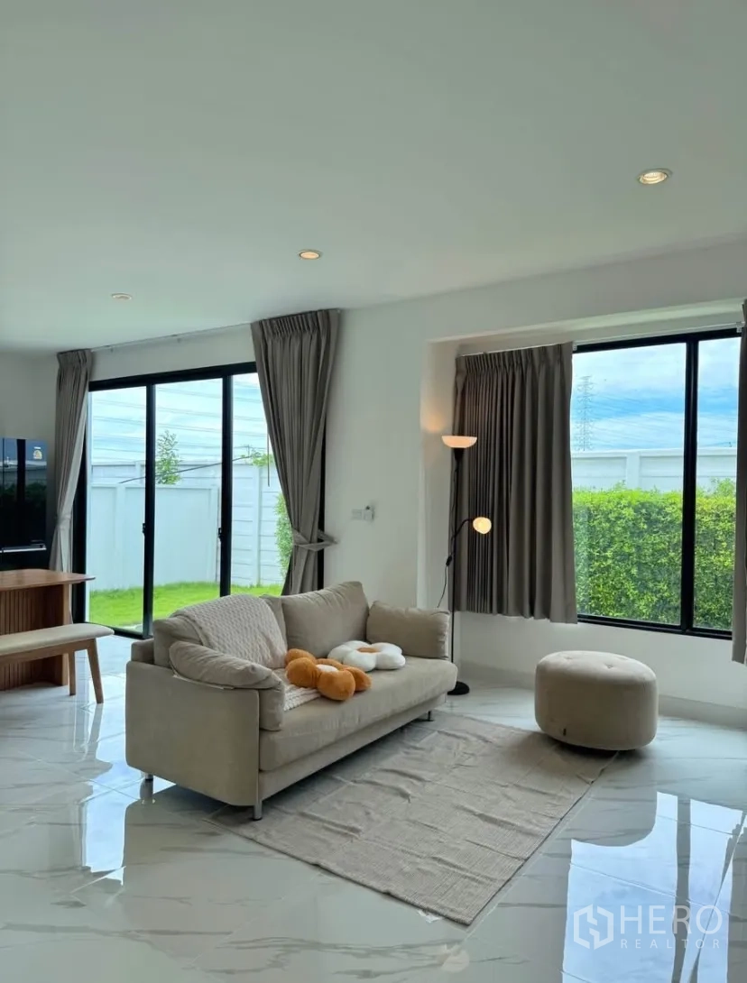 Detached House for rent in Samut Prakan - Open-plan lounge with large windows, gray curtains and glossy floor tiles.