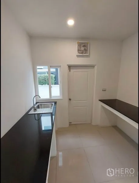 Detached House for sale in Bang Yai, Nonthaburi - Bright galley kitchen with black stone countertops, sink, window and back door