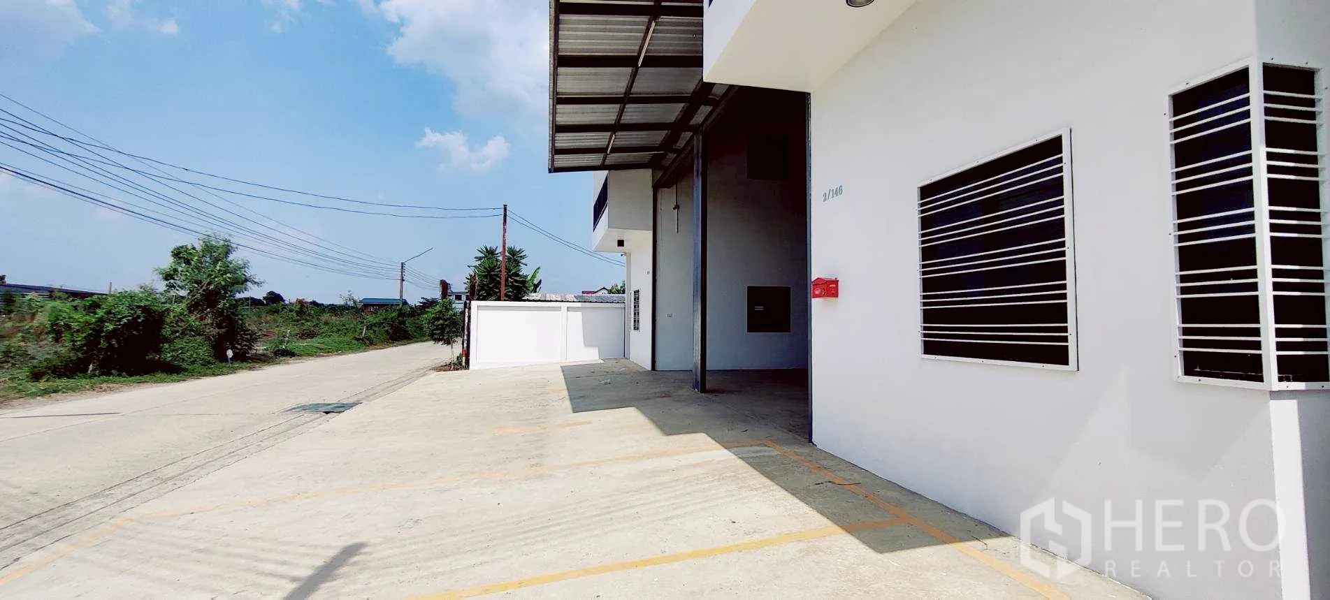 Warehouse for rent in Lam Luk Ka, Pathum Thani - Concrete driveway and covered loading bay beside the warehouse on a wide access road.