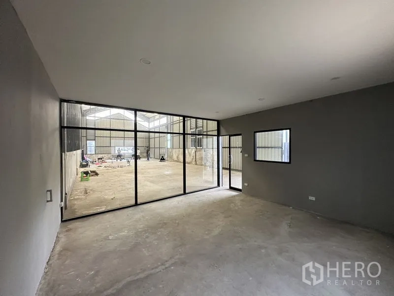 Warehouse for rent in Lat Phrao, Bangkok - Office room with full-height glass wall facing the warehouse floor and grey walls.