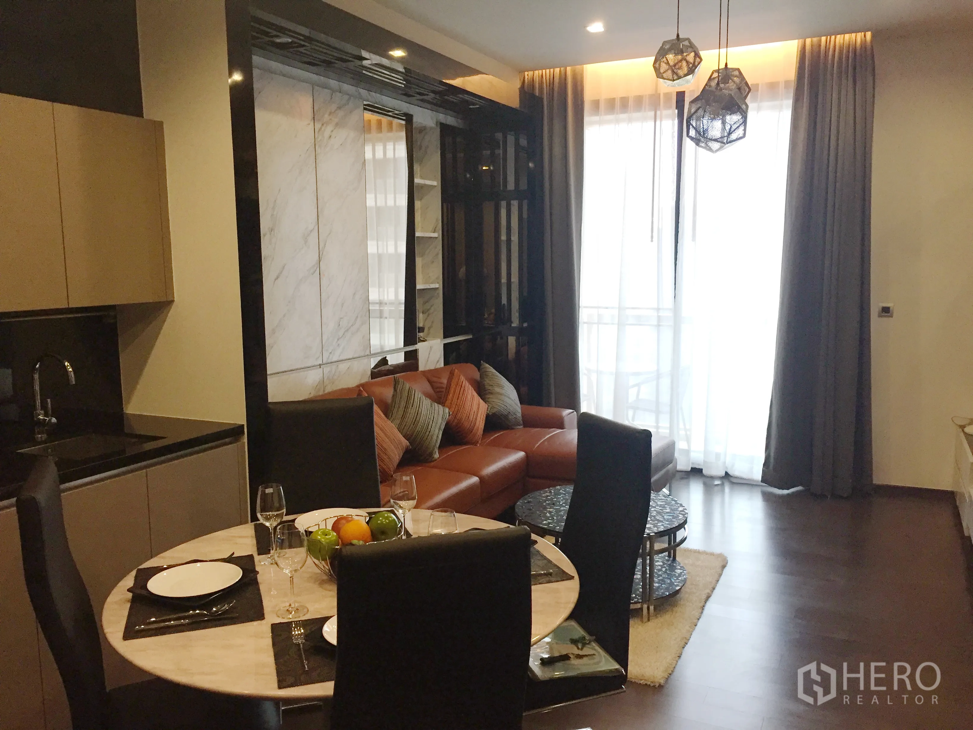 Condominium for rent in Watthana, Bangkok - Open-plan living and dining area with pendant lights, leather sofa, balcony access and full-height curtains.