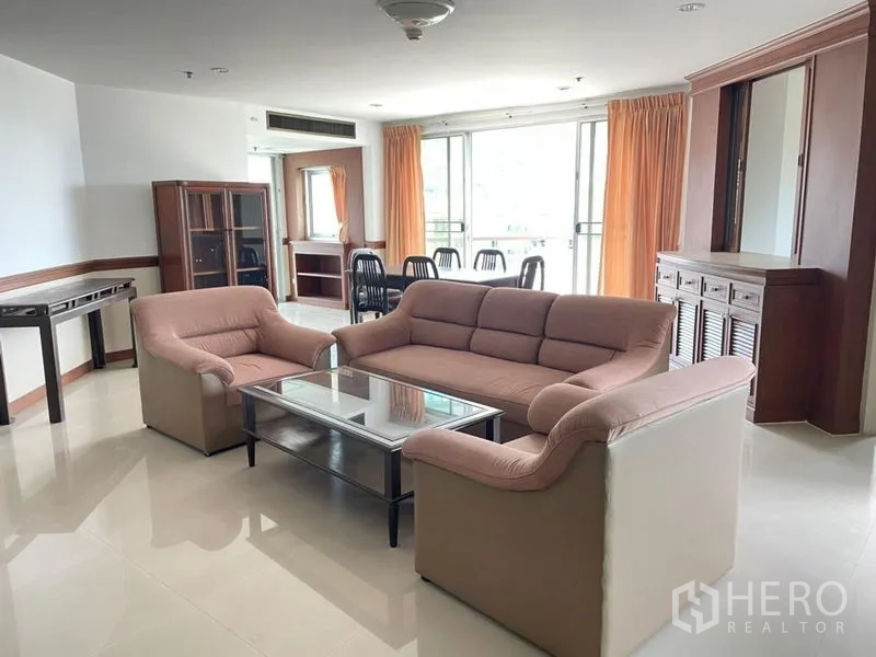 Condominium for rent in Khlong Toei, Bangkok - Open living room with sofa set, glass coffee table, and sliding doors to the balcony.