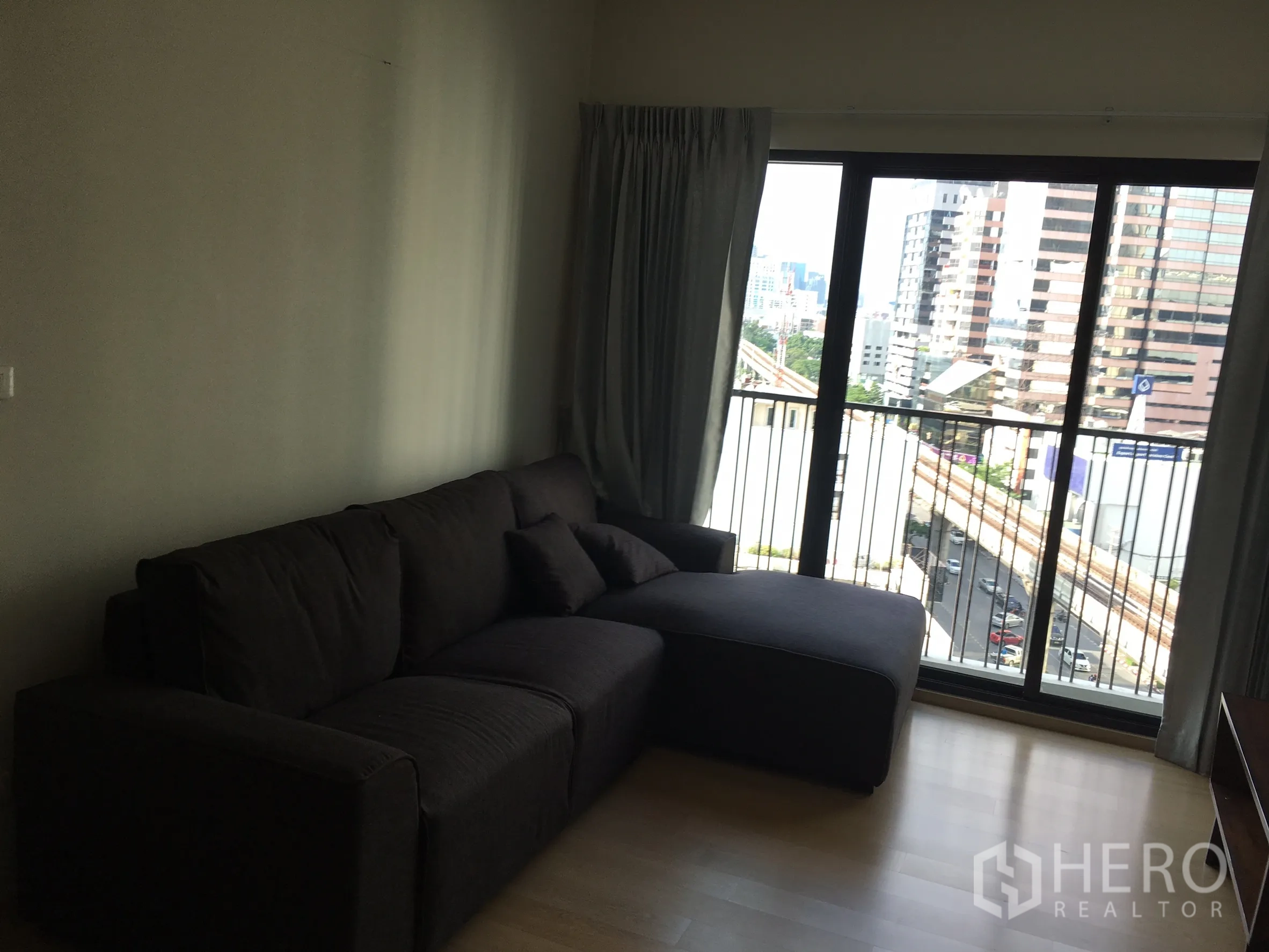 Condominium for rent in Phaya Thai, Bangkok - Living room with dark sectional sofa opening to a balcony with city view near BTS.