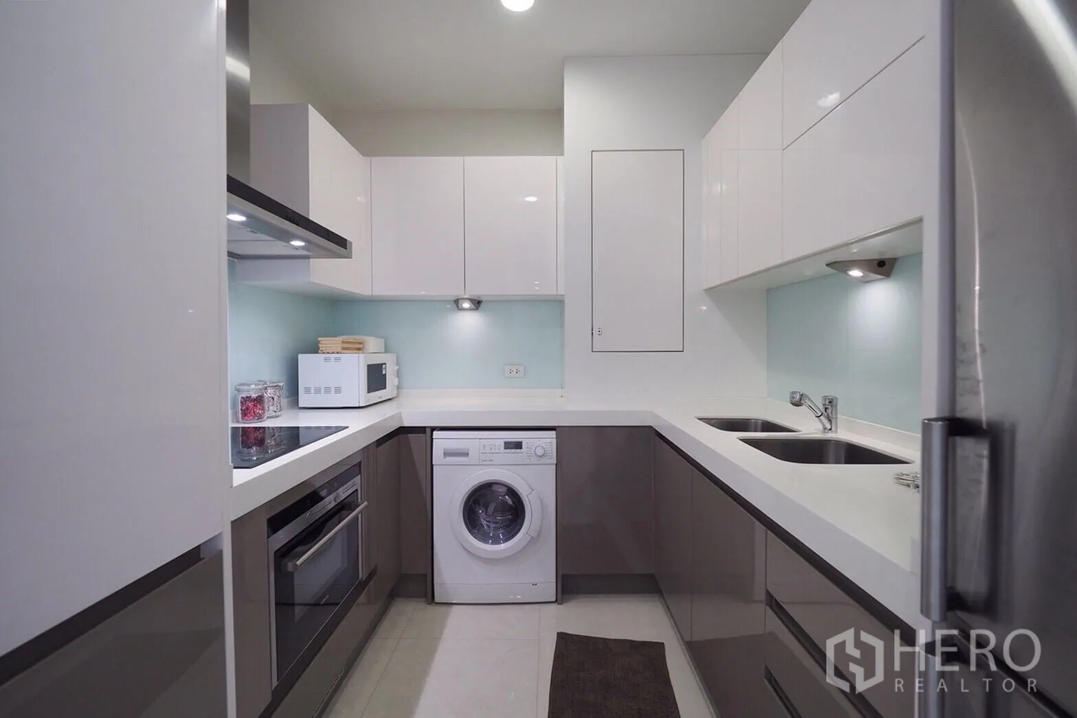 Condominium for rent in Pathum Wan, Bangkok - U-shaped kitchen with glossy cabinets, oven, microwave, double sink and washing machine.