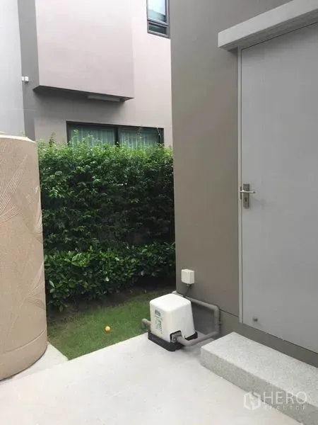 独立式住宅 出售在Pak Kret, Nonthaburi - 侧门与台阶，设备泵及绿篱小庭院
