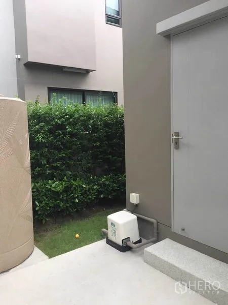 独立式住宅 出售在Pak Kret, Nonthaburi - 侧门与台阶，设备泵及绿篱小庭院
