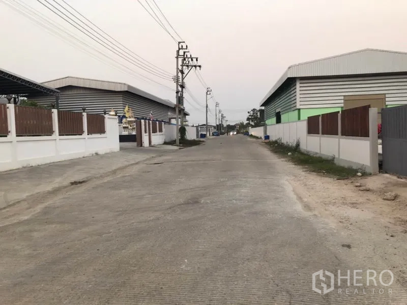 Factory for sale in Pak Kret, Nonthaburi - Quiet industrial street lined with modern warehouse buildings and utility poles.