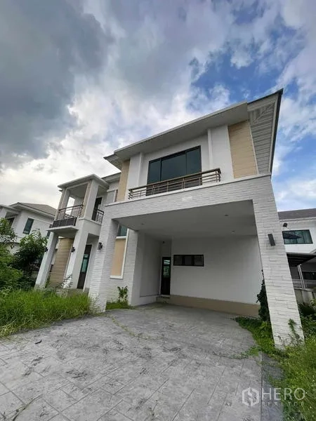 独立式住宅 出售在Lat Krabang, Bangkok - 外立面展示带顶双车位车棚和铺装车道，周围绿化。