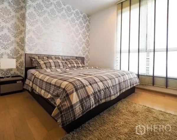 Condominium for rent in Watthana, Bangkok - Bedroom with large bed, accent wallpaper, hardwood floors, and full-height windows.
