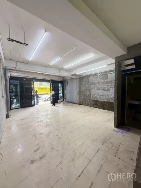 Shophouse for rent in Khlong Toei, Bangkok - Ground-floor retail space with wide glass storefront and bright fluorescent lighting facing the street.