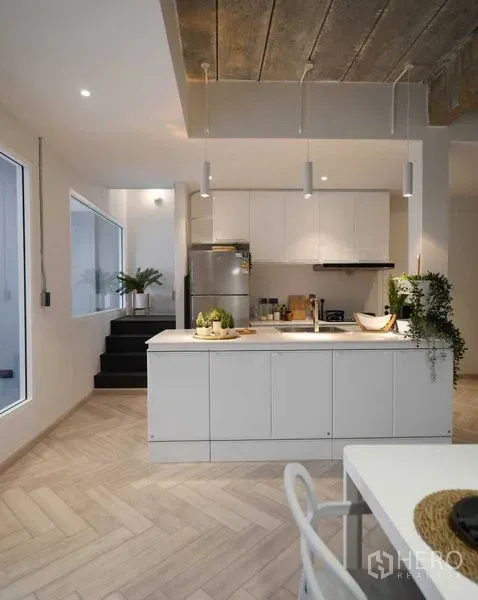 Townhouse for rent in Watthana, Bangkok - Modern white kitchen with island, pendant lighting, built-in cabinets and stair access.