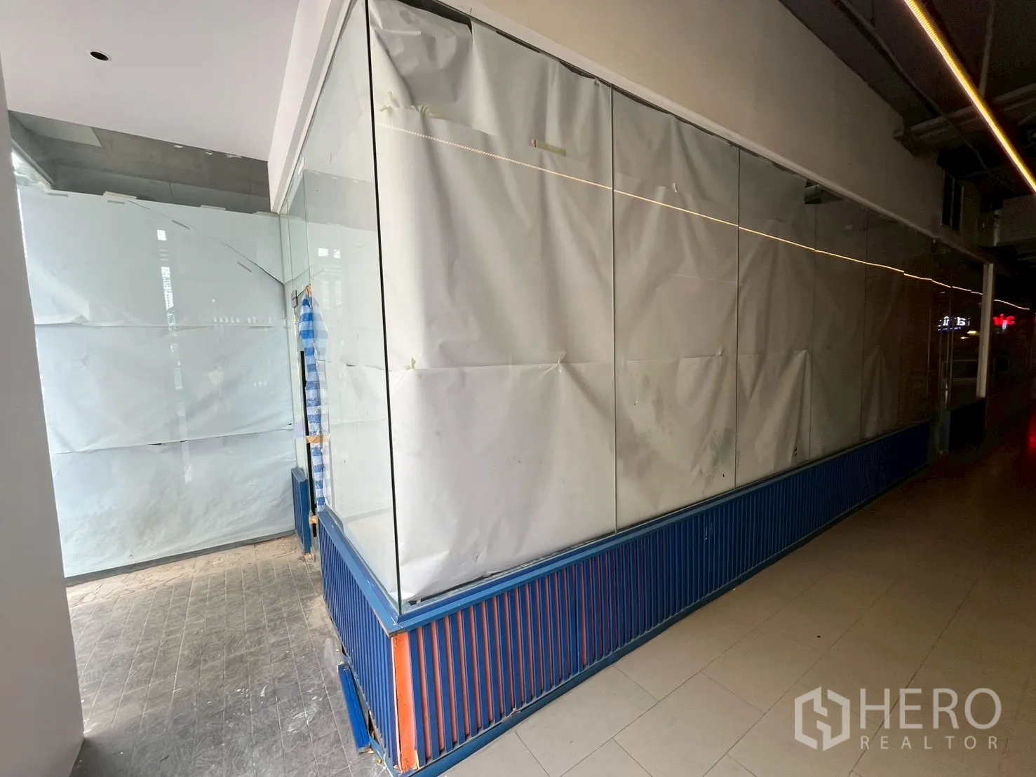 พื้นที่ขายของ for rent in Watthana, Bangkok - หน้าร้านกระจกยาวติดทางเดินภายในอาคาร กระดาษปิดหน้าต่าง ฐานซี่สีน้ำเงิน พื้นกระเบื้อง พร้อมไฟเส้นบนเพดาน