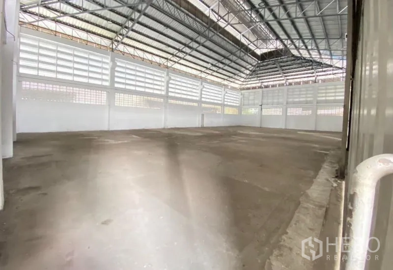 Warehouse for rent or sale in Mueang Samut Sakhon, Samut Sakhon - Spacious warehouse interior featuring a high steel truss roof, ventilated walls, and a concrete floor.