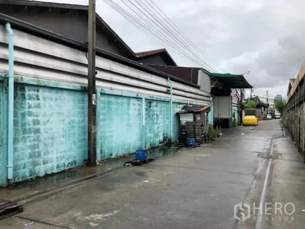 Warehouse for rent in Bang Kho Laem, Bangkok - Exterior service lane beside a warehouse complex with turquoise block wall and truck access.