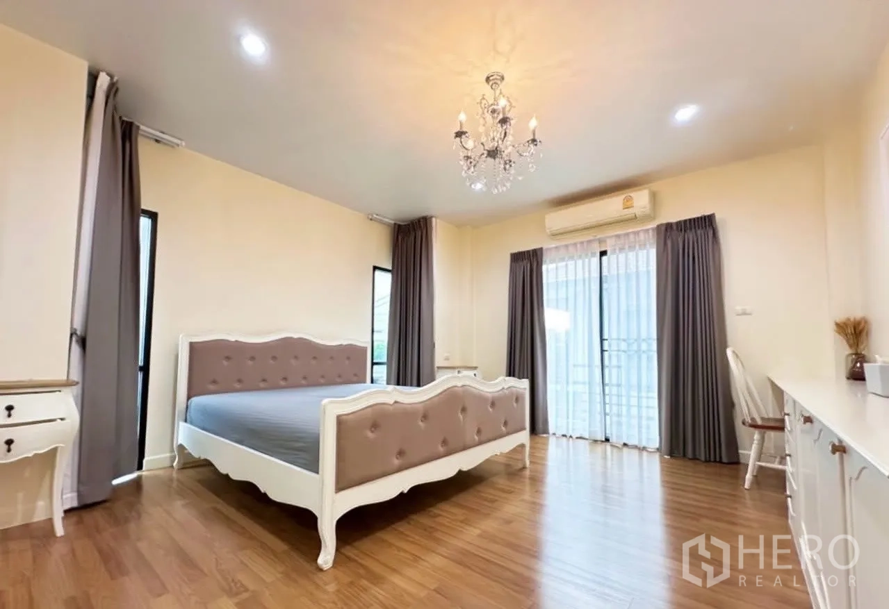 Detached House for sale in Lam Luk Ka, Pathum Thani - Master bedroom with chandelier, classic bed frame, balcony door and wood flooring.