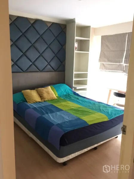 Condominium for rent in Khlong Toei, Bangkok - Master bedroom with padded blue feature headboard, large bed, and built-in shelving.