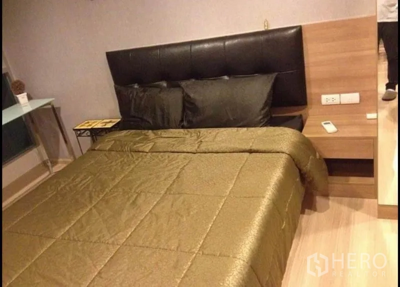 Condominium for sale in Phaya Thai, Bangkok - Bedroom with padded headboard, bedside table, gold duvet and wooden flooring.