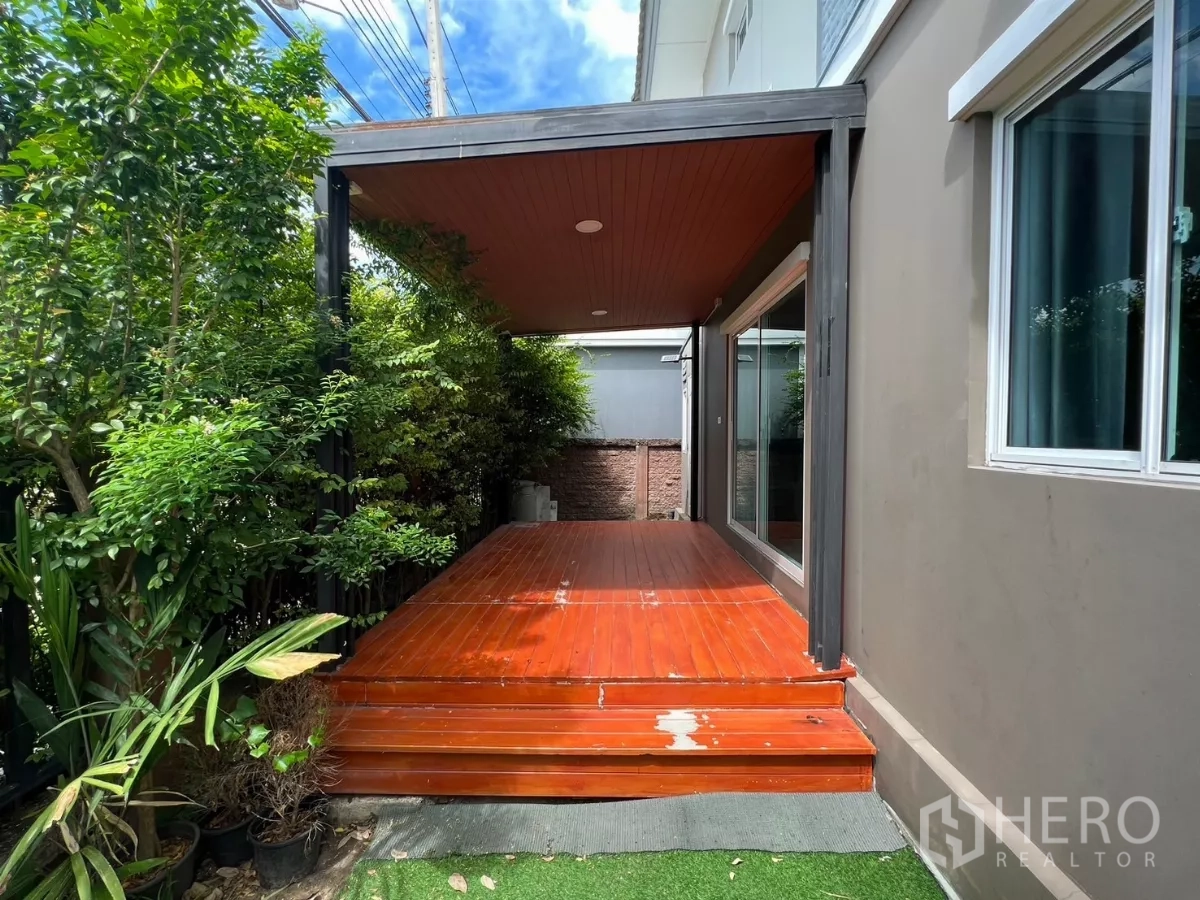 独立式住宅 出租在Suan Luang, Bangkok - 房侧带屋顶的木质露台，旁有绿植与推拉玻璃门