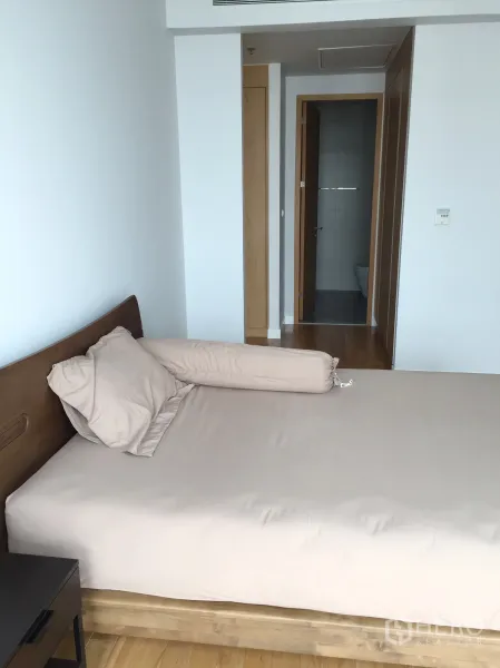 Condominium for rent in Khlong Toei, Bangkok - Primary bedroom with wood bedframe and direct access to an ensuite bathroom.