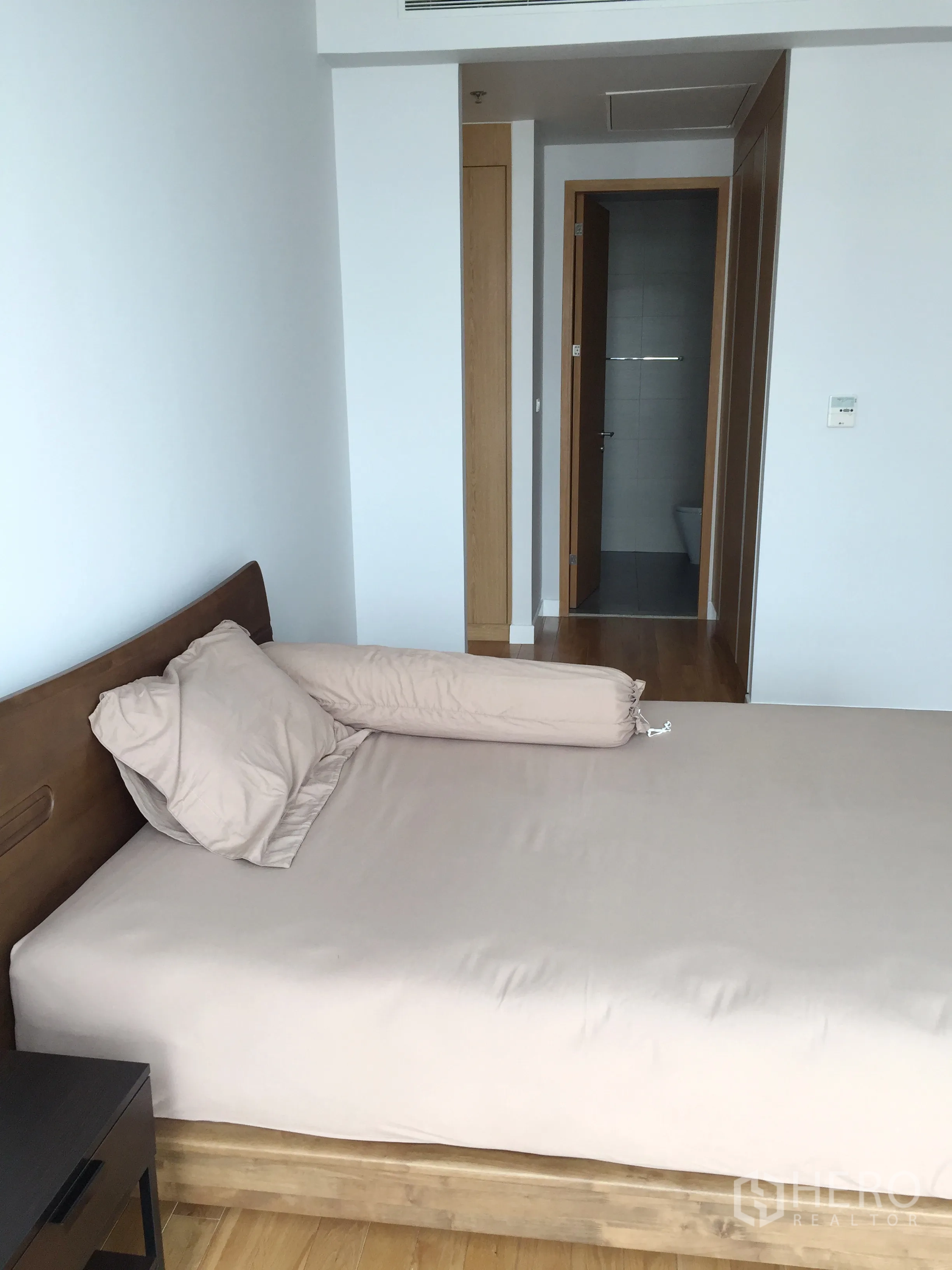 Condominium for rent in Khlong Toei, Bangkok - Primary bedroom with wood bedframe and direct access to an ensuite bathroom.