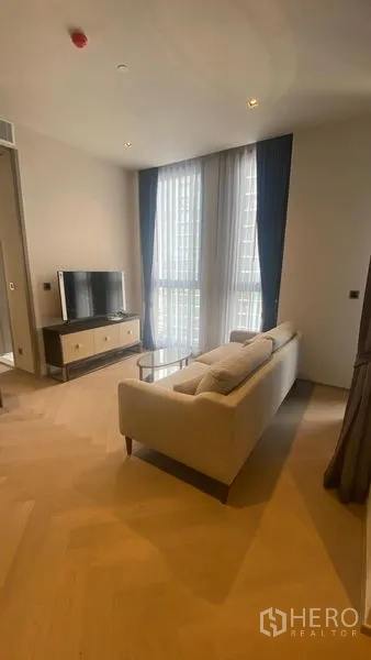 Condominium for rent - Cozy lounge with sofa facing TV, tall windows and warm wood floors.