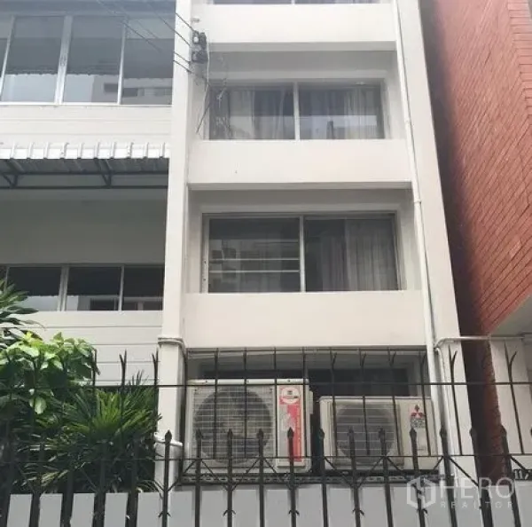 Townhouse for rent in Watthana, Bangkok - Front facade of a multi-storey white townhouse in Watthana with a metal fence and outdoor air-conditioning units.