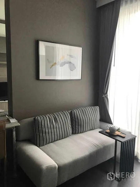 Condominium for rent in Watthana, Bangkok - Sofa corner with striped cushions, wall art, and a side table by a sunlit window.
