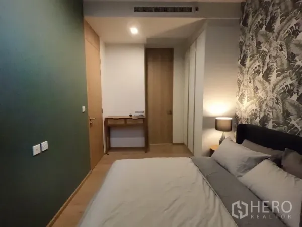 Condominium for rent in Watthana, Bangkok - Cozy bedroom with double bed, feature wallpaper, green accent wall, built-in wardrobe and small writing desk.