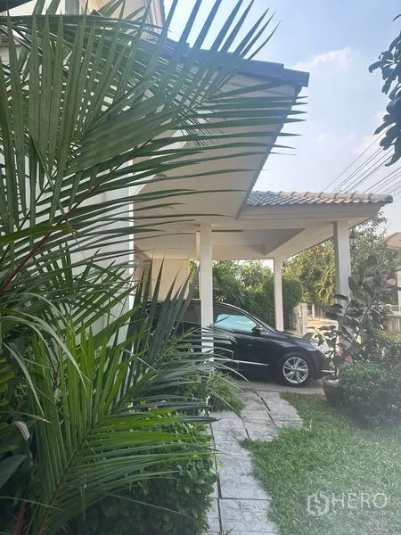 Detached House for rent in Bang Phli, Samut Prakan - Covered carport along the side of the house bordered by tropical plants.