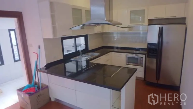 Detached House for rent in Watthana, Bangkok - Modern U-shaped kitchen with black granite countertops, range hood, and stainless appliances.
