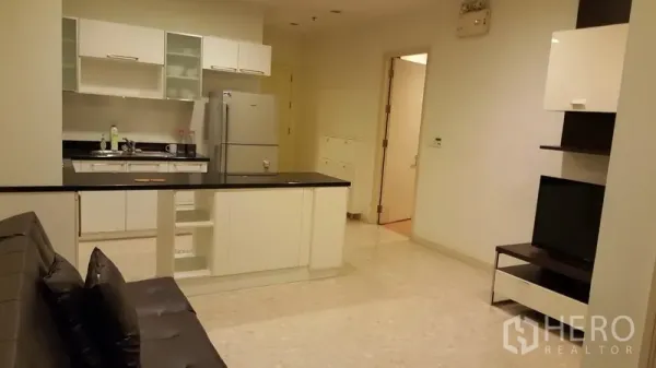 Condominium for rent in Khlong Toei, Bangkok - Open-plan living area with white kitchen, breakfast counter, refrigerator and sofa.