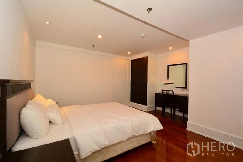 Apartment for rent in Khlong Toei, Bangkok - Cozy bedroom with double bed, recessed lights, work desk and wardrobe on warm wood floors.