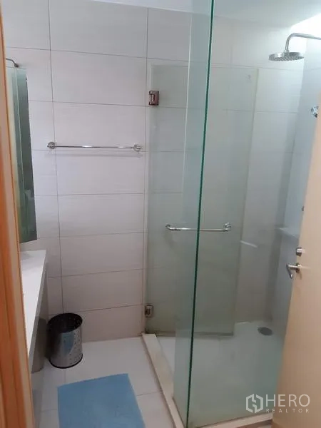 Condominium for rent in Khlong Toei, Bangkok - Contemporary bathroom with a glass-enclosed shower, rain shower head, and white tiled walls.