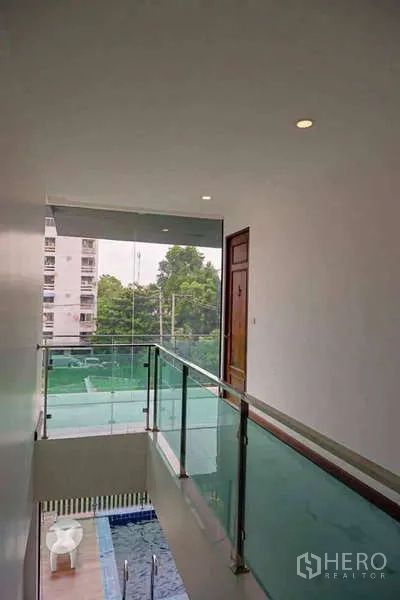 独立式住宅 出售在Lat Phrao, Bangkok - 二层过道玻璃栏杆，可俯视泳池与社区。